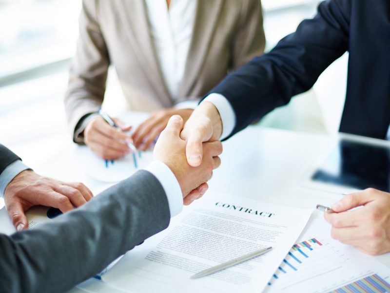 Image of business partners handshaking over business objects on workplace